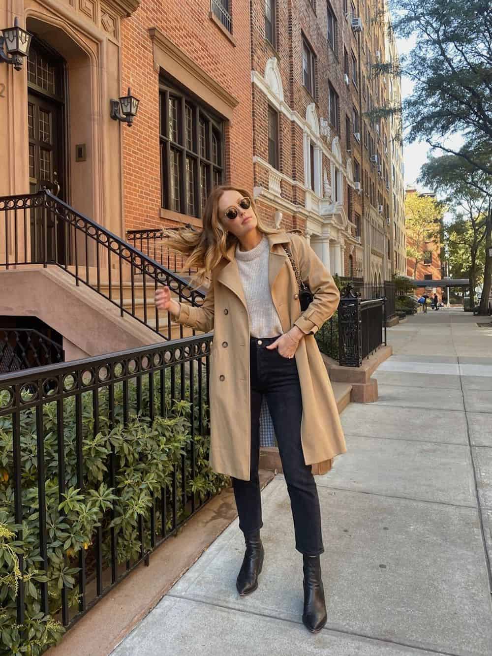 Woman wearing black jeans, black boots, a grey sweater and a tan trench coat.