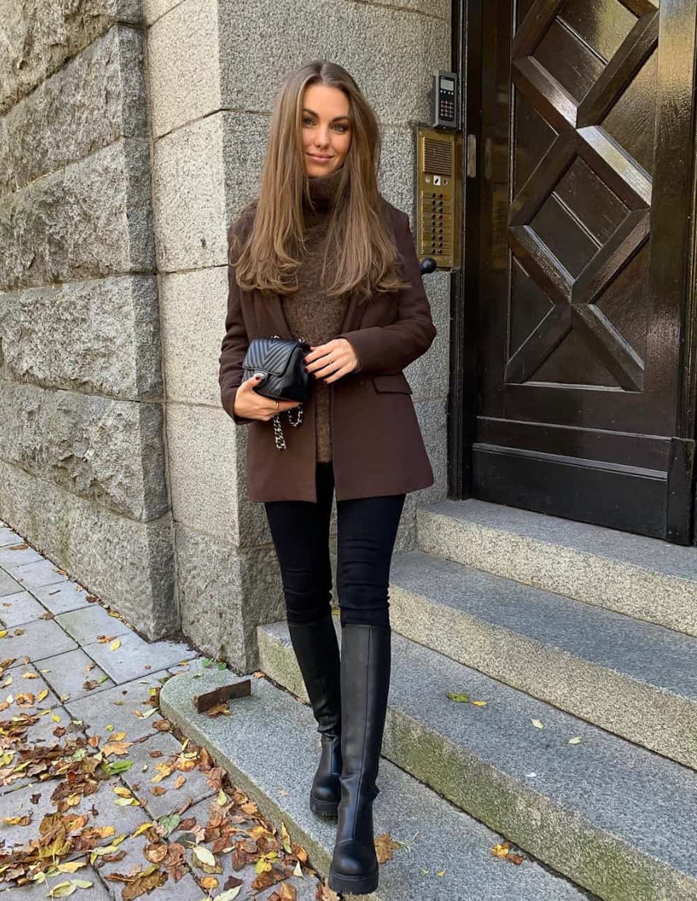 Woman wearing black leggings, black riding boots, a brown blazer coat and a brown sweater.