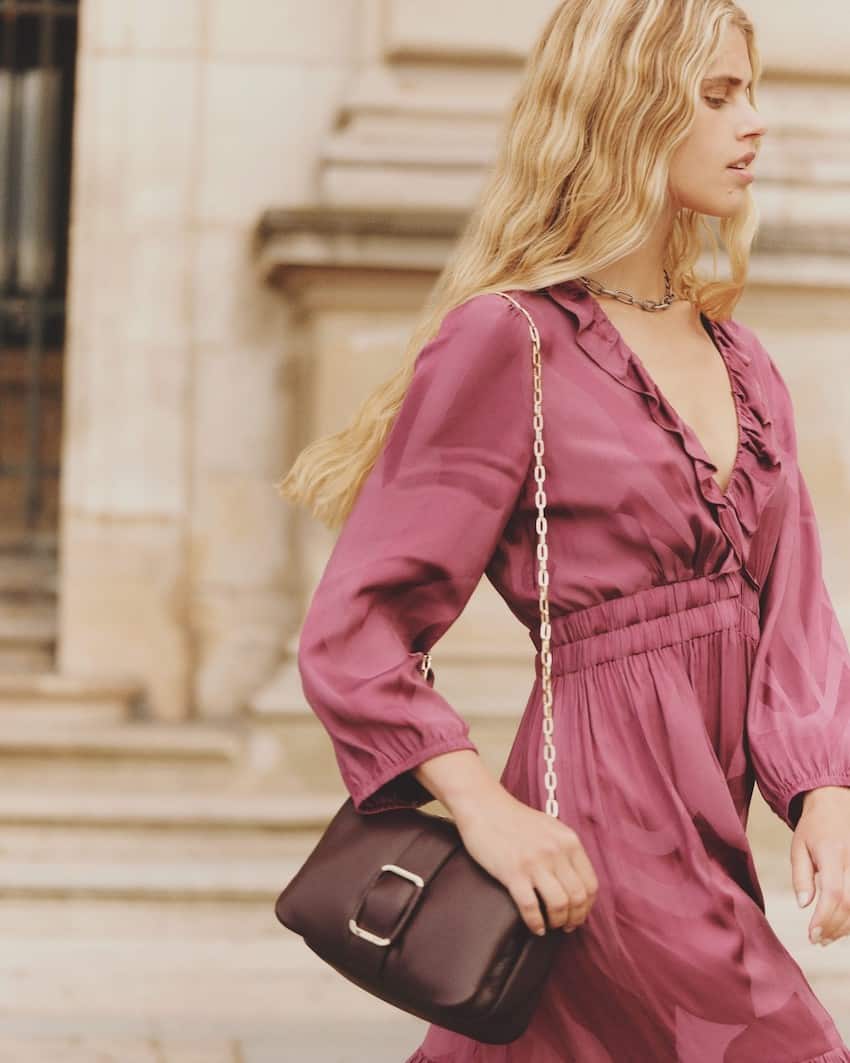 Woman wearing a wine colored dress with a Burgundy handbag.