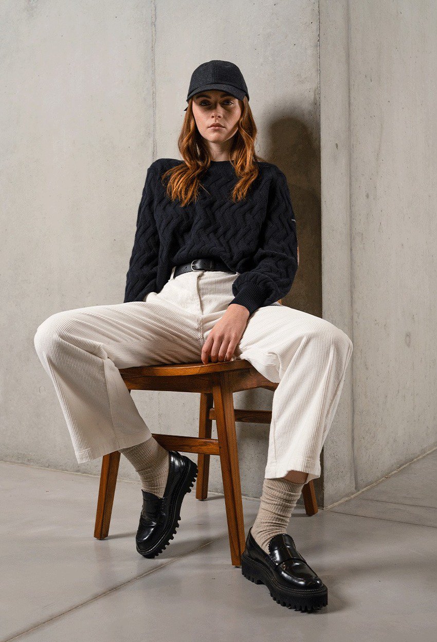 Woman wearing white pants with black clogs and a black sweater.