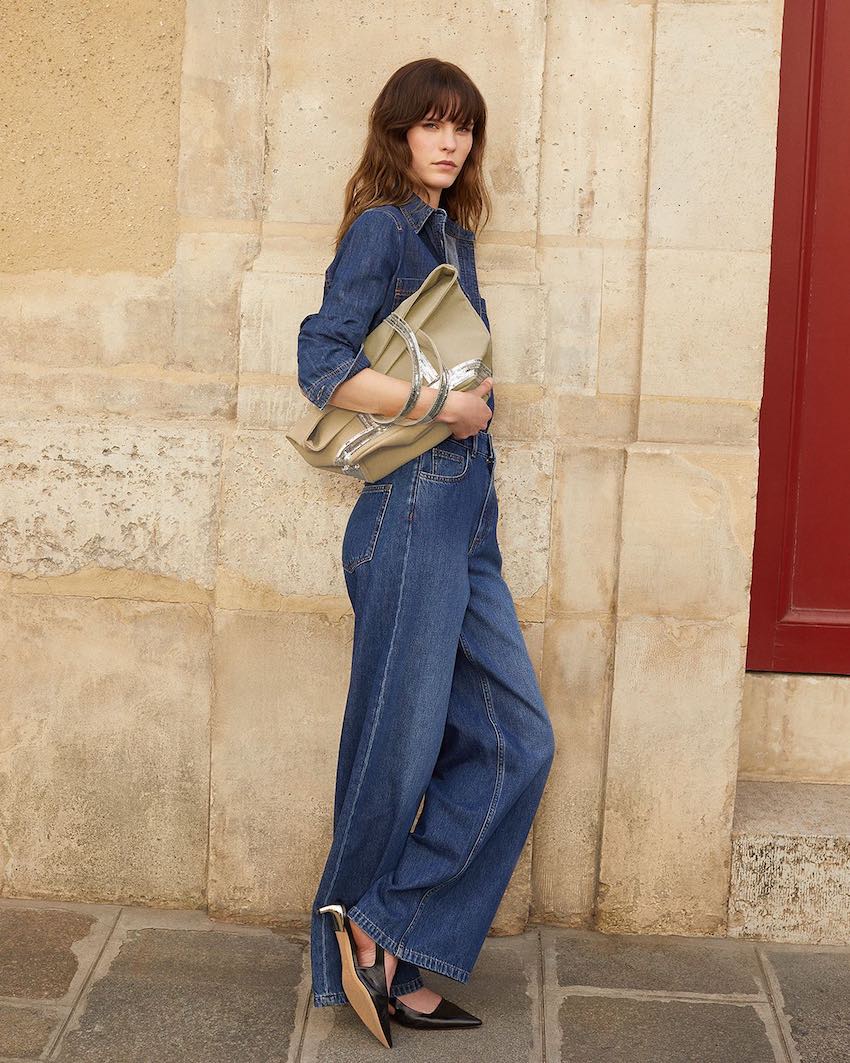Woman wearing a denim jumpsuit with black flats.