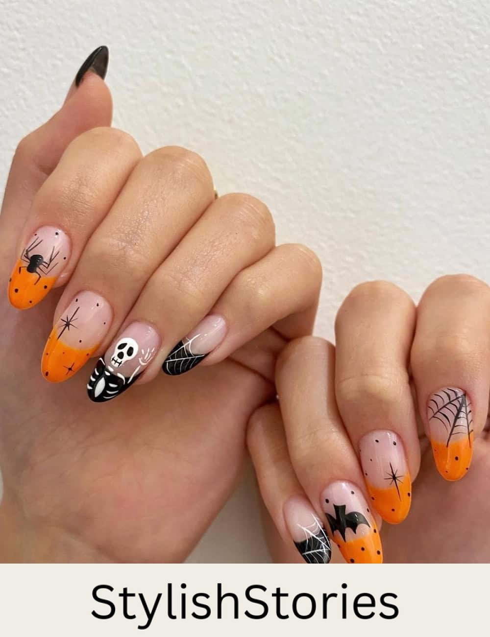 long nude almond nails with black and orange tips and Halloween nail art featuring skeletons, spiders, and bats