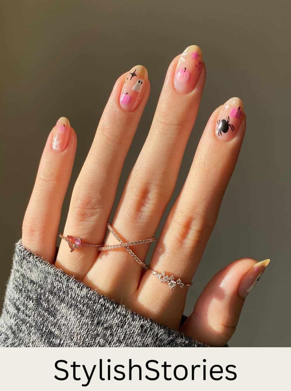 short nude almond nails with white, black, and pink polish featuring spiders, ghosts, pumpkins, and webs
