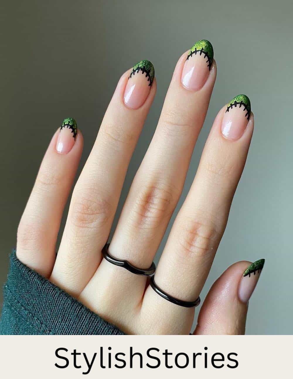 short nude almond nails with shimmering green tips and black stitched borders
