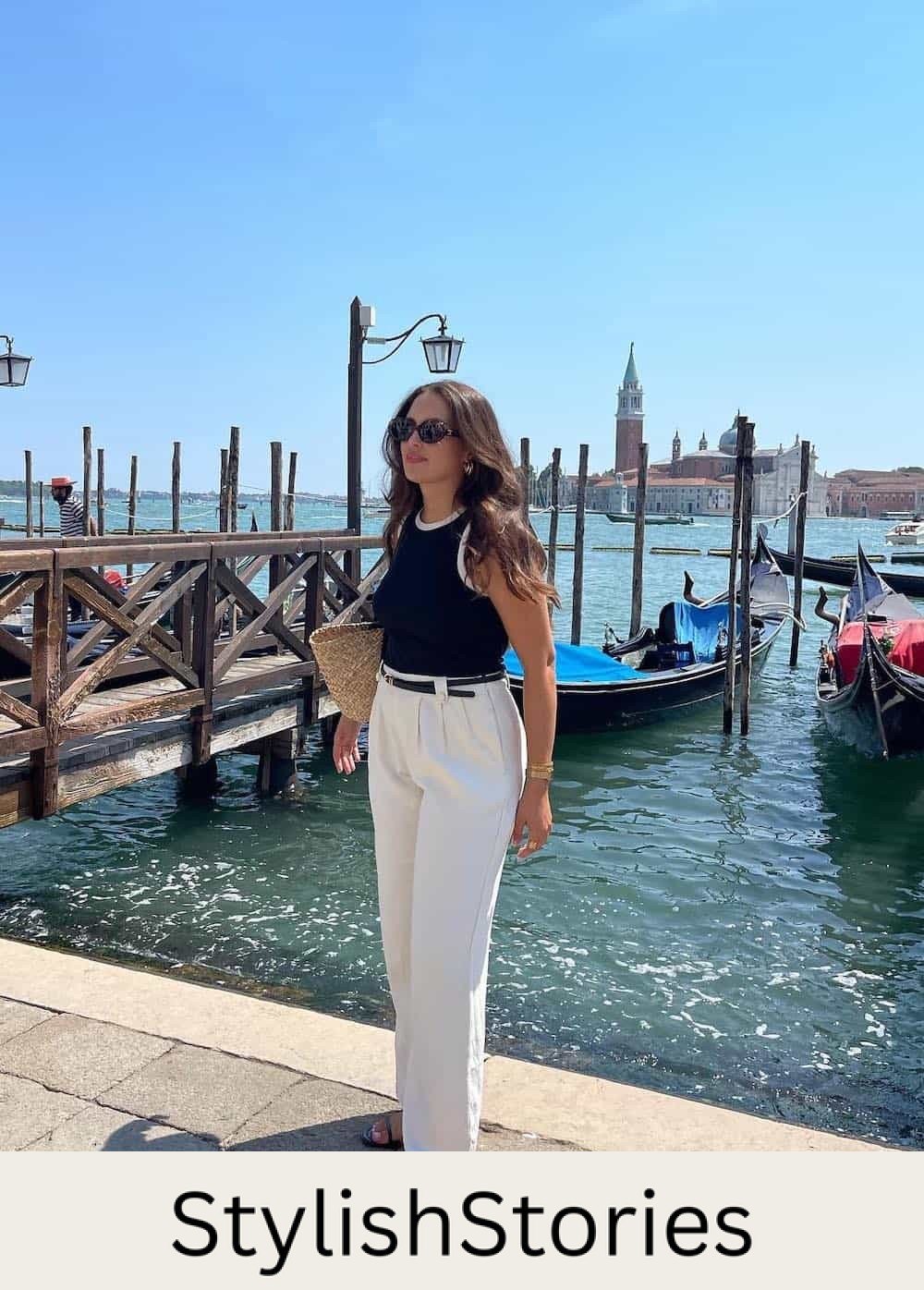 Woman wearing white trousers, a black and white tank top and black sandals.