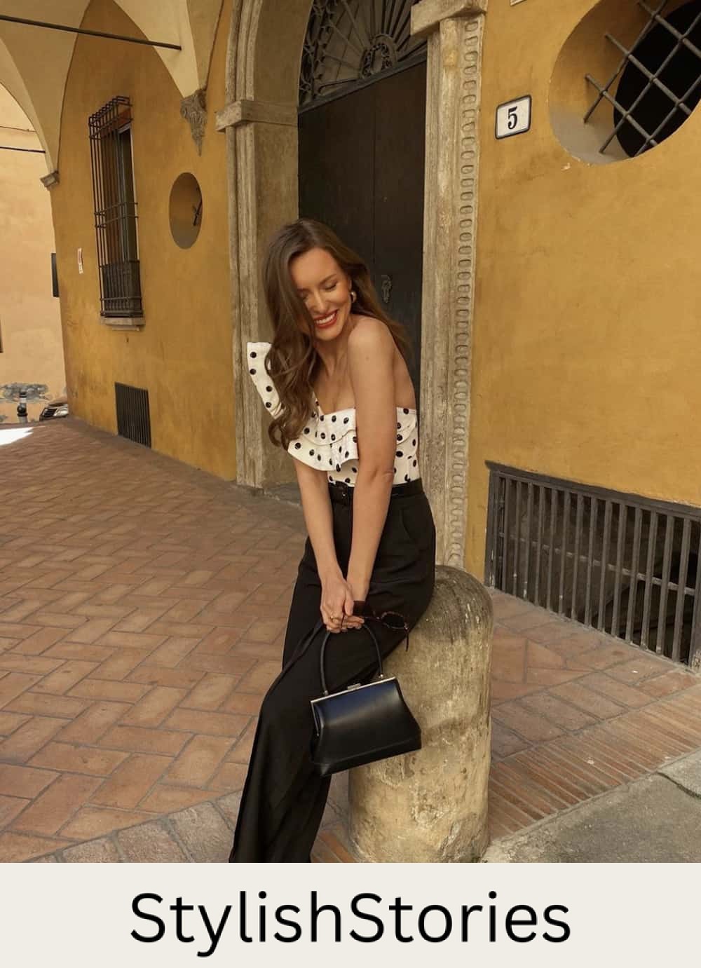 Woman wearing black trousers and a black and white polka dot ruffle top with black heels.