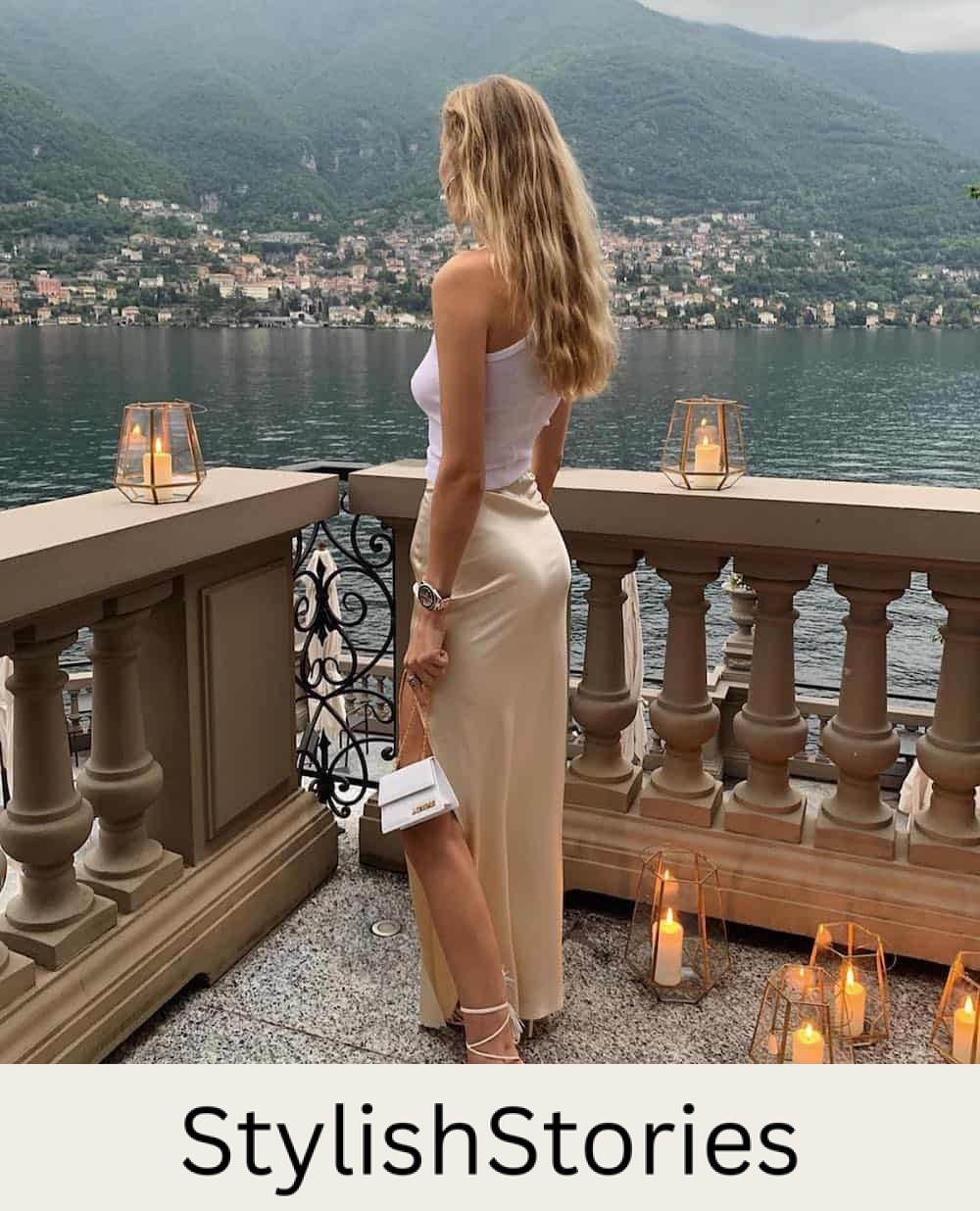 Woman wearing a silk midi skirt with a white tank top and white heels.