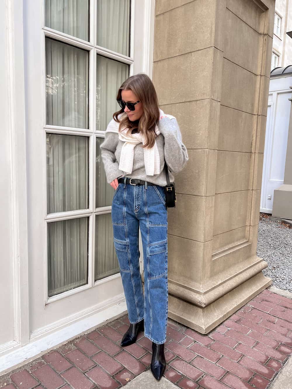 woman wearing a grey fuzzy cashmere Lilysilk pullover sweater with blue cargo jeans and black boots and an ivory sweater over her shoulders