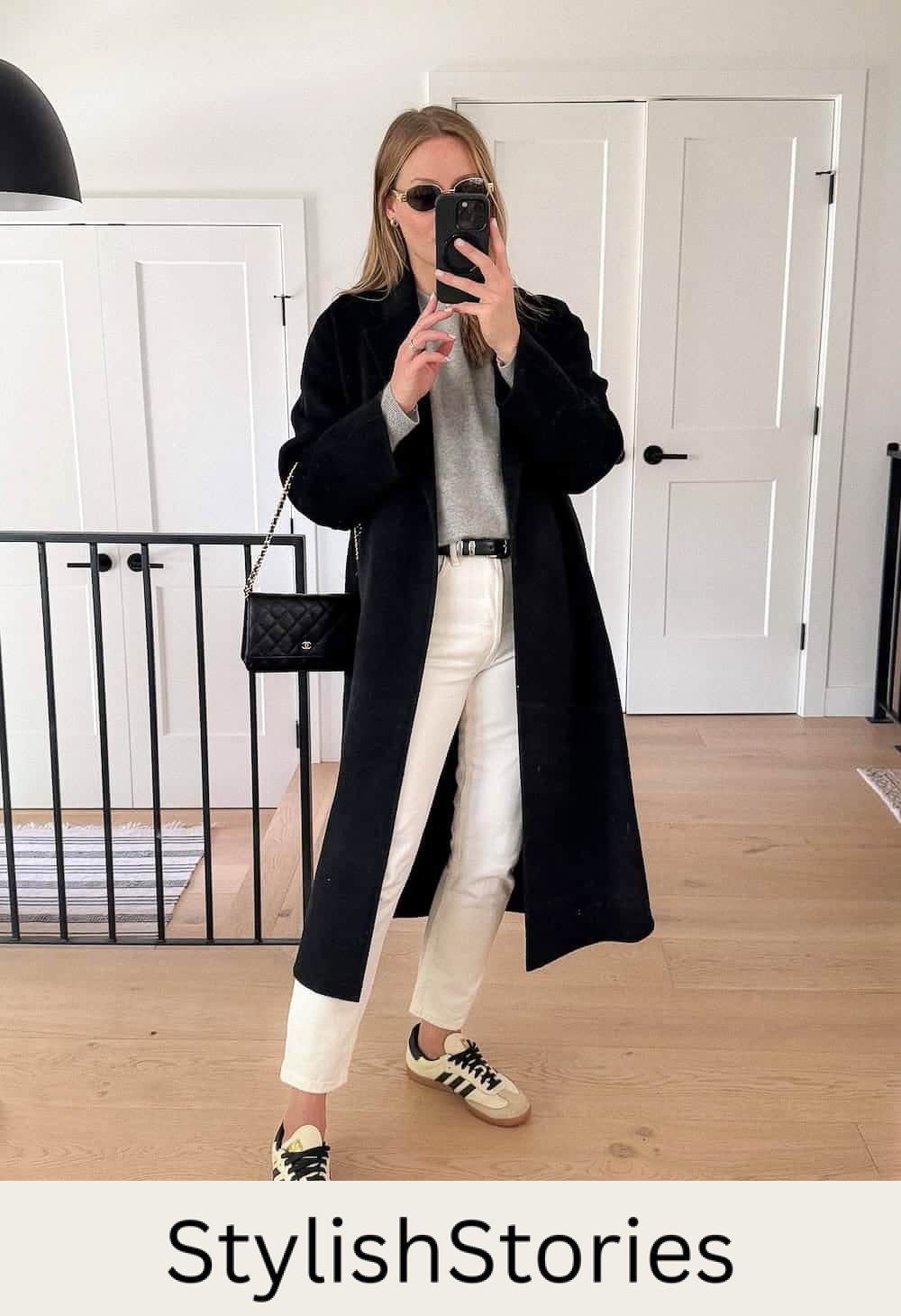 Christal wearing white jeans, sneakers, a grey sweater and a long black coat.