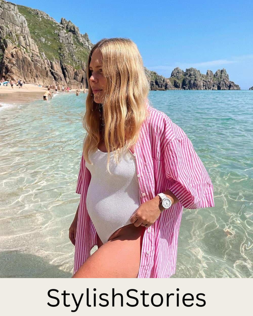 Pregnant woman wearing a white swimsuit with a striped pink button-up shirt over top
