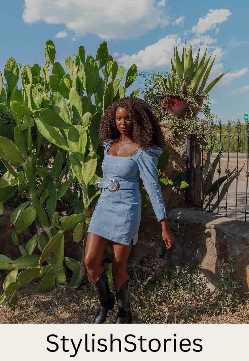 A woman wearing a belted denim mini dress with long puffed sleeves and black cowboy boots