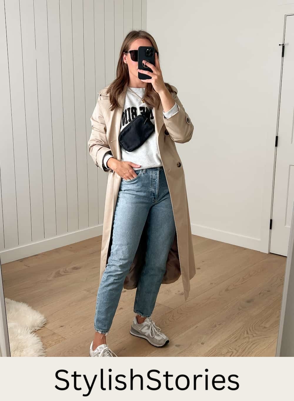woman wearing a long tan trench coat over a grey sweatshirt and jeans with white New Balance sneakers