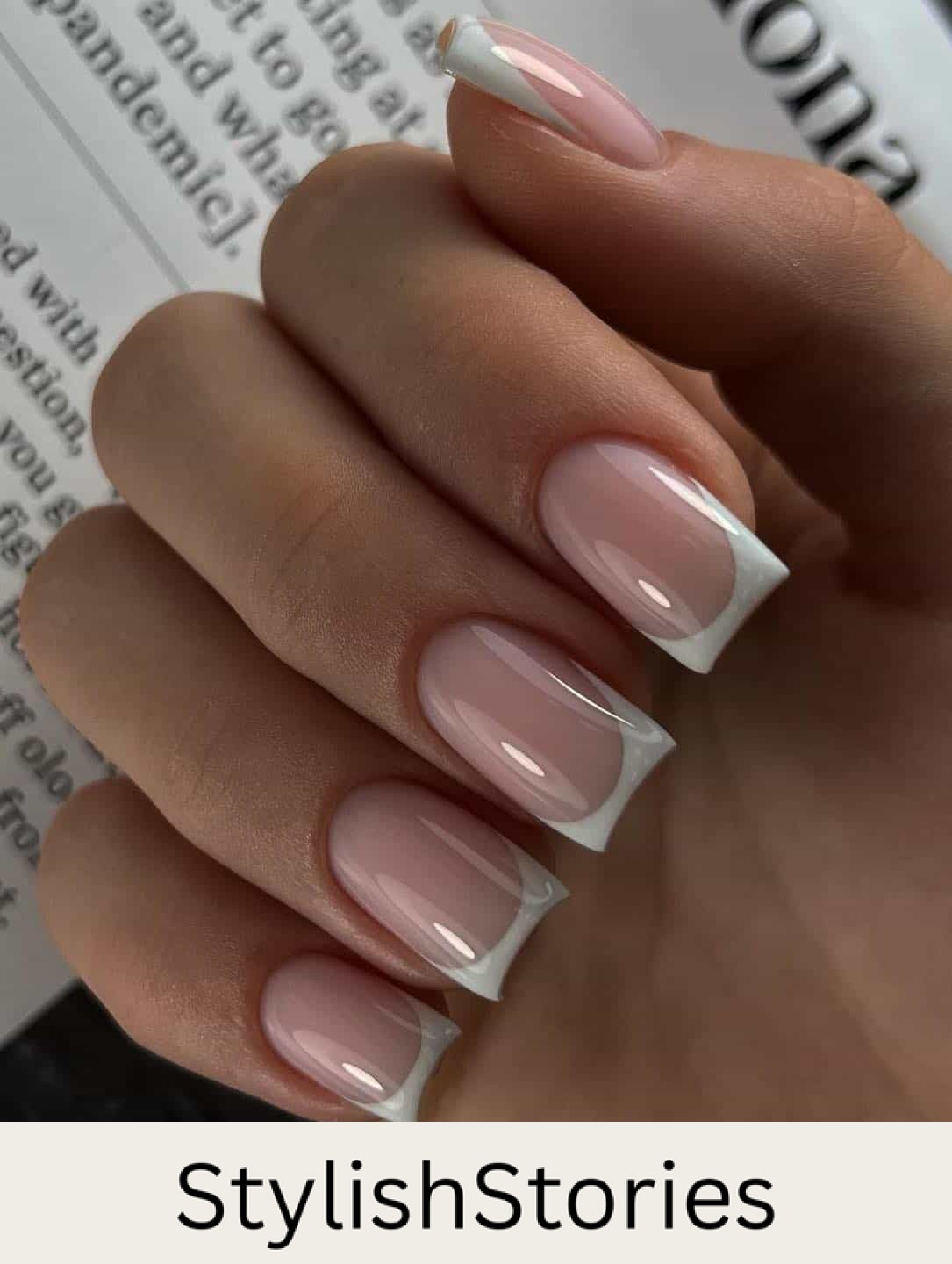 A hand with medium light pink square nails with white tips and a glossy finish