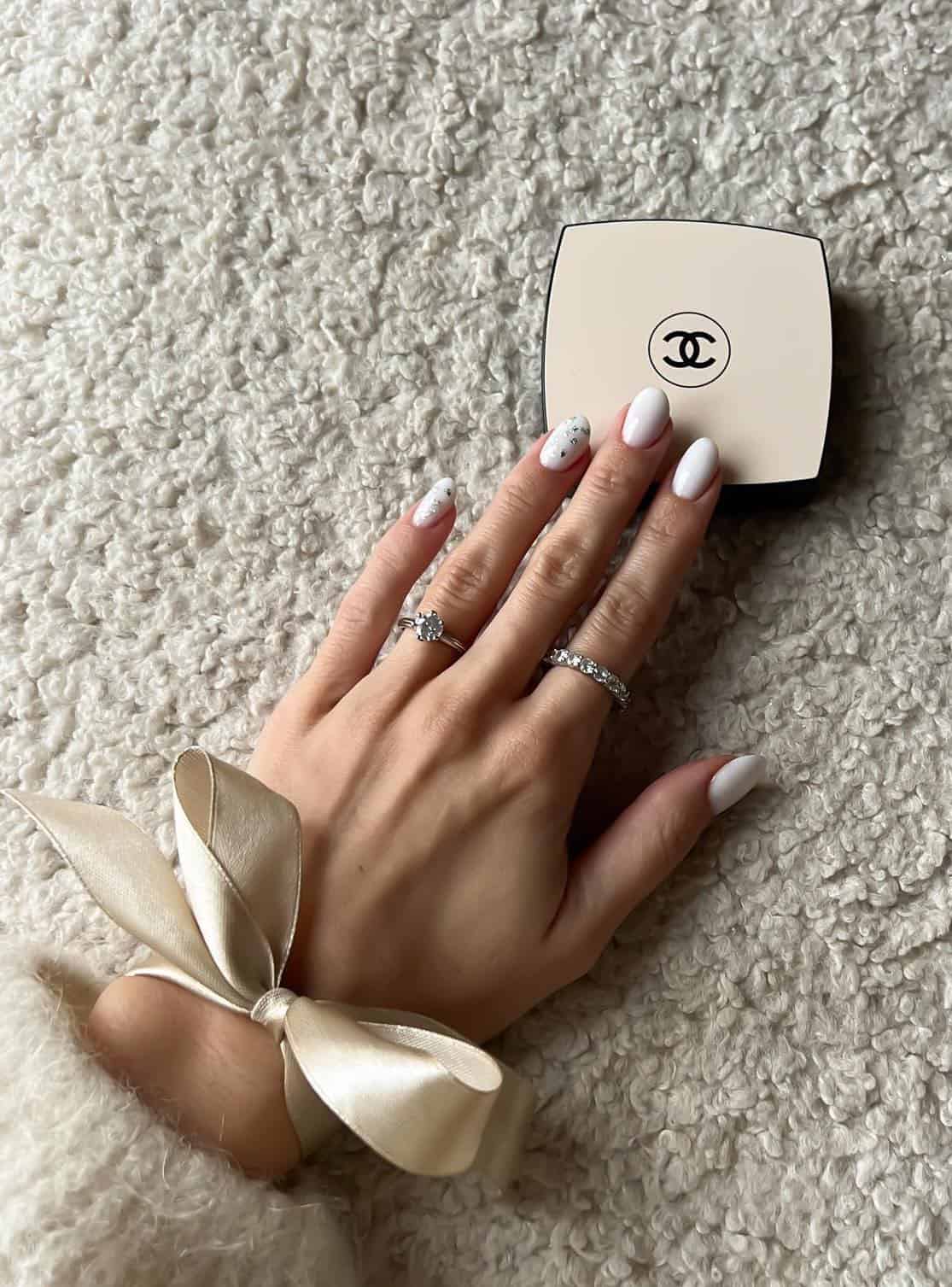 A hand with short round nails painted a white polish and two accent nails with silver flakes