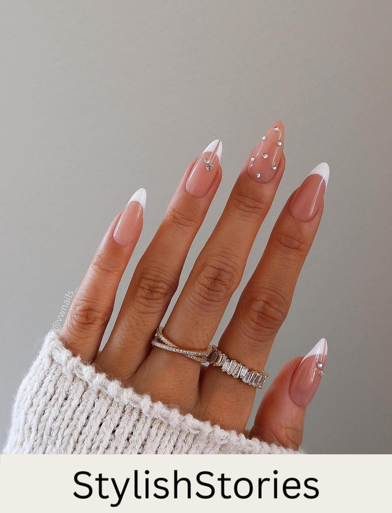 A hand with medium nude almond nails with white tips and crystal details