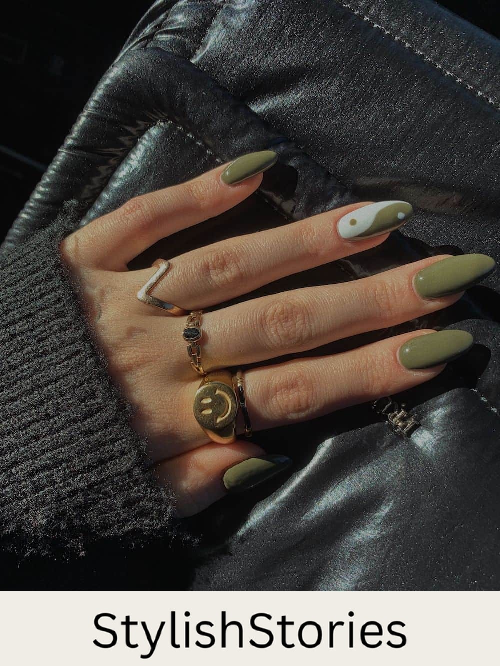hand with long almond nails with olive green polish and a ying-yang accent nail