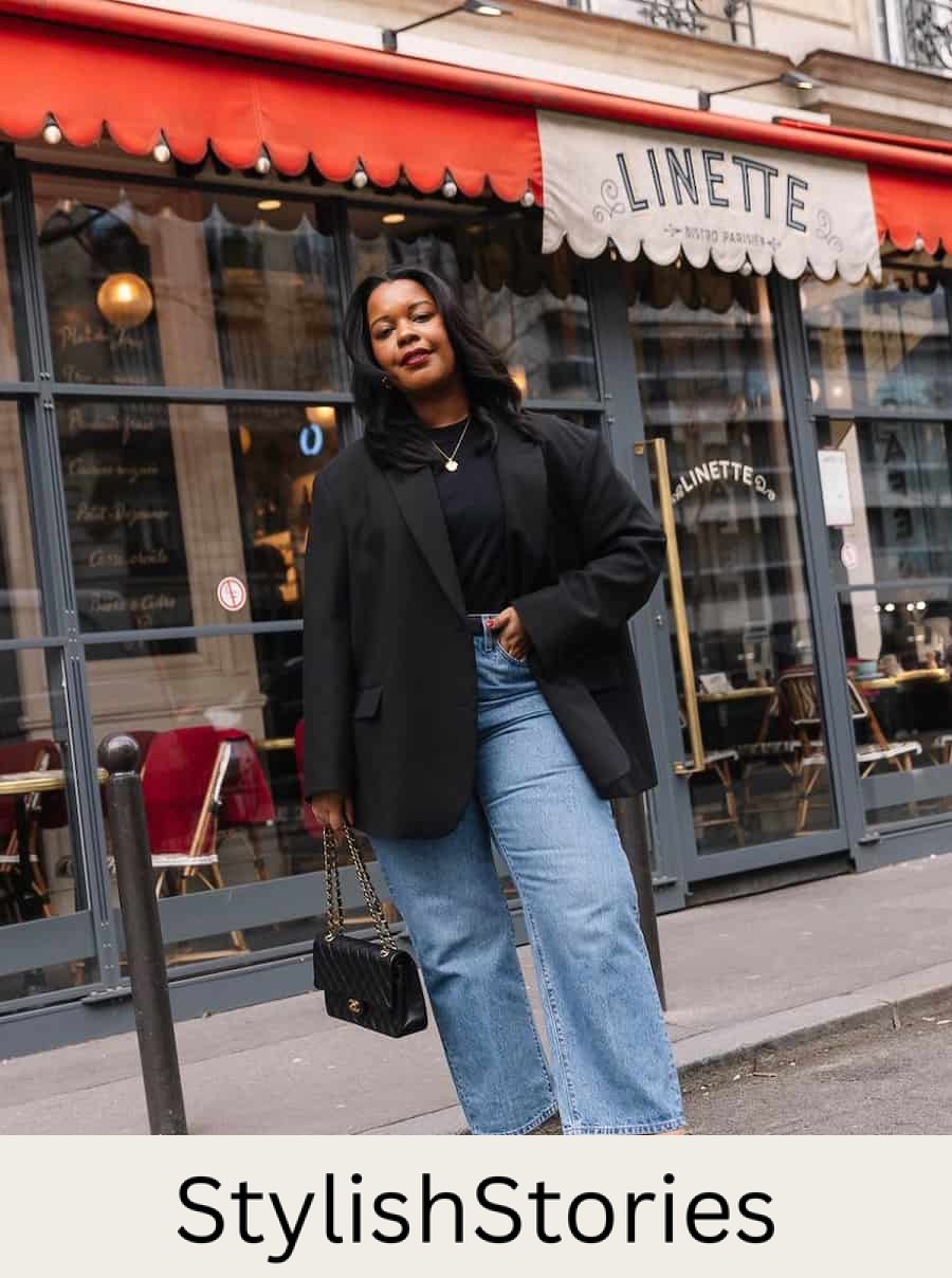 A woman wearing light washed jeans with a black tee, a black blazer, black heels, and a black shoulder bag