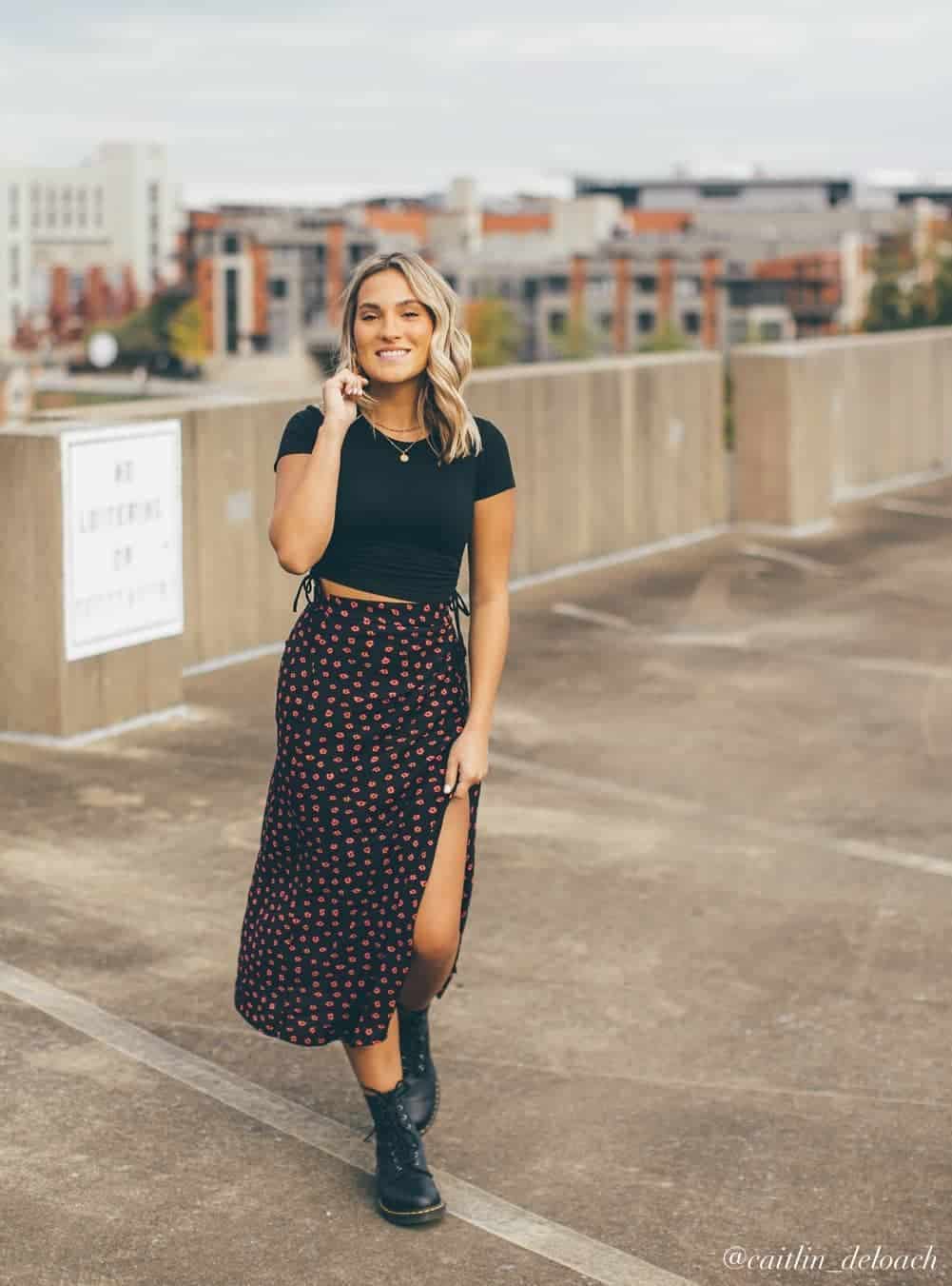 young woman wearing a black cropped t-shirt with a black and red patterned midi skirt and combat boots for senior pictures