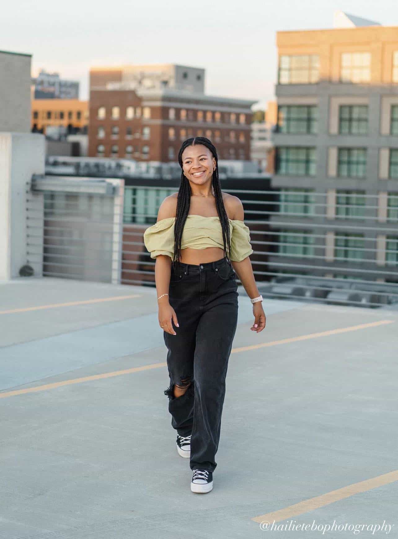 young black woman wearing a green cropped off-the-shoulder top with baggy black jeans and sneakers for senior pictures