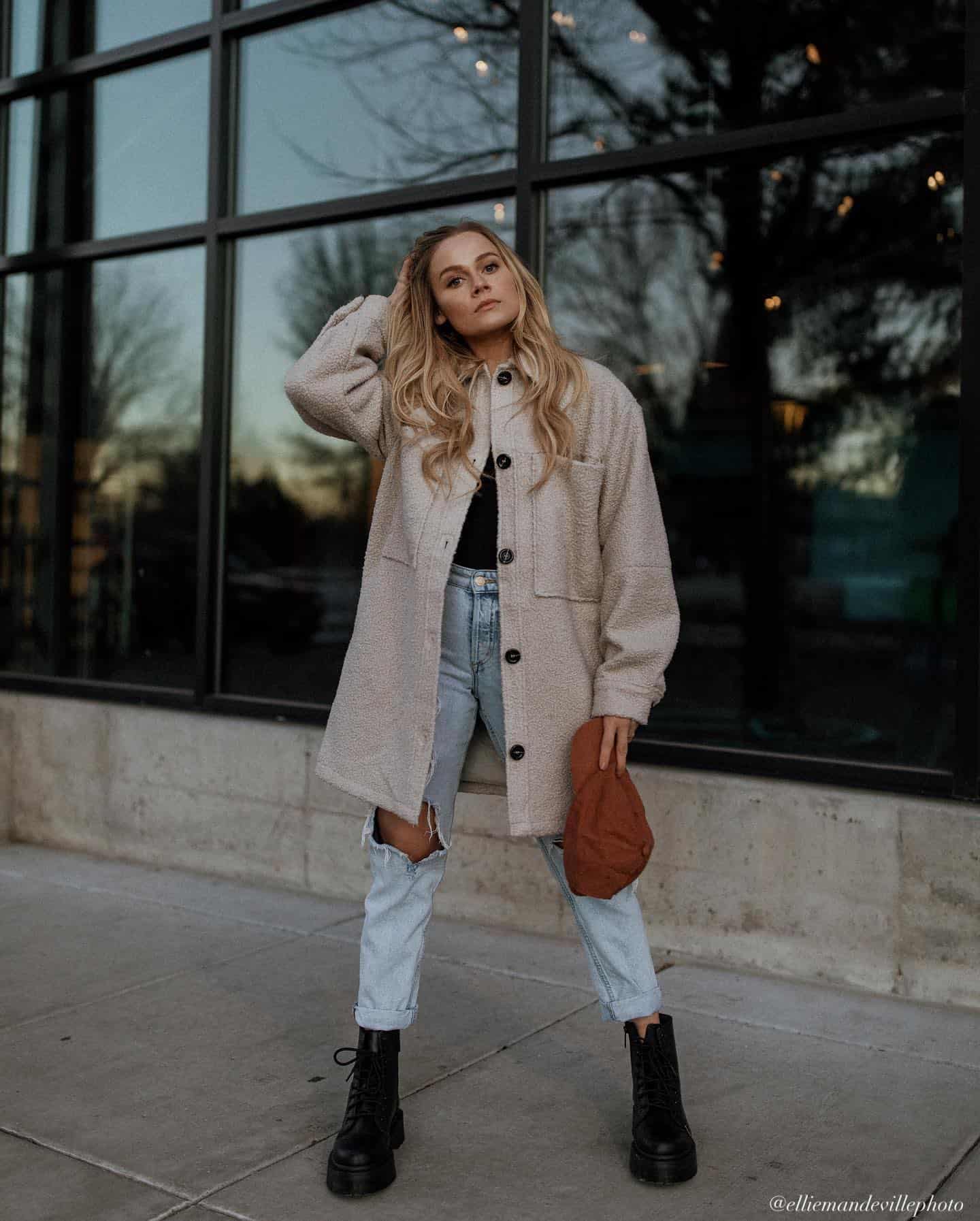 young woman wearing a beige shirt jacket with light blue jeans and black boots for Senior pictures