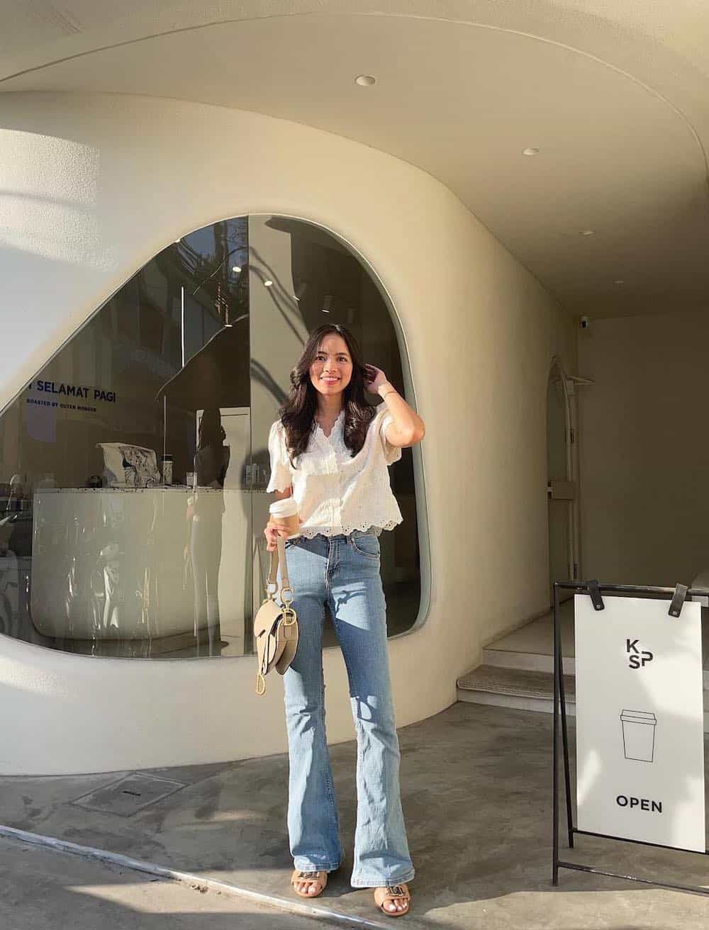 woman wearing a white blouse with full-length blue flared jeans and heeled beige sandals