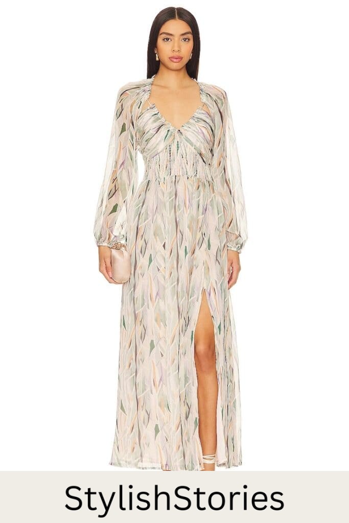 A woman wearing a v-neck maxi dress with sheer long puffed sleeves, a side slit on the front, with a pastel green, purple, and orange pattern