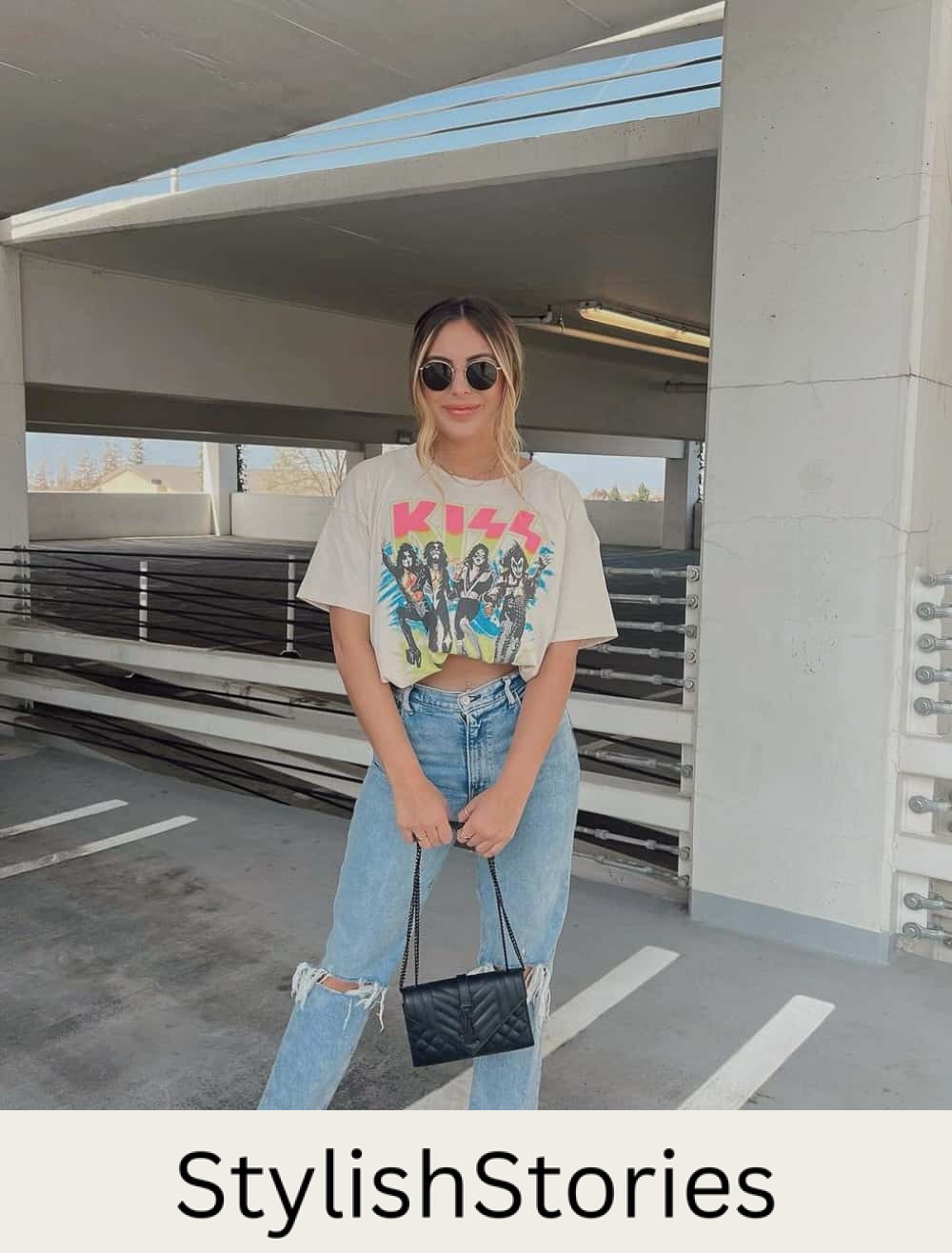 A woman wearing a graphic tee, ripped blue jeans, and pink heels with a black handbag