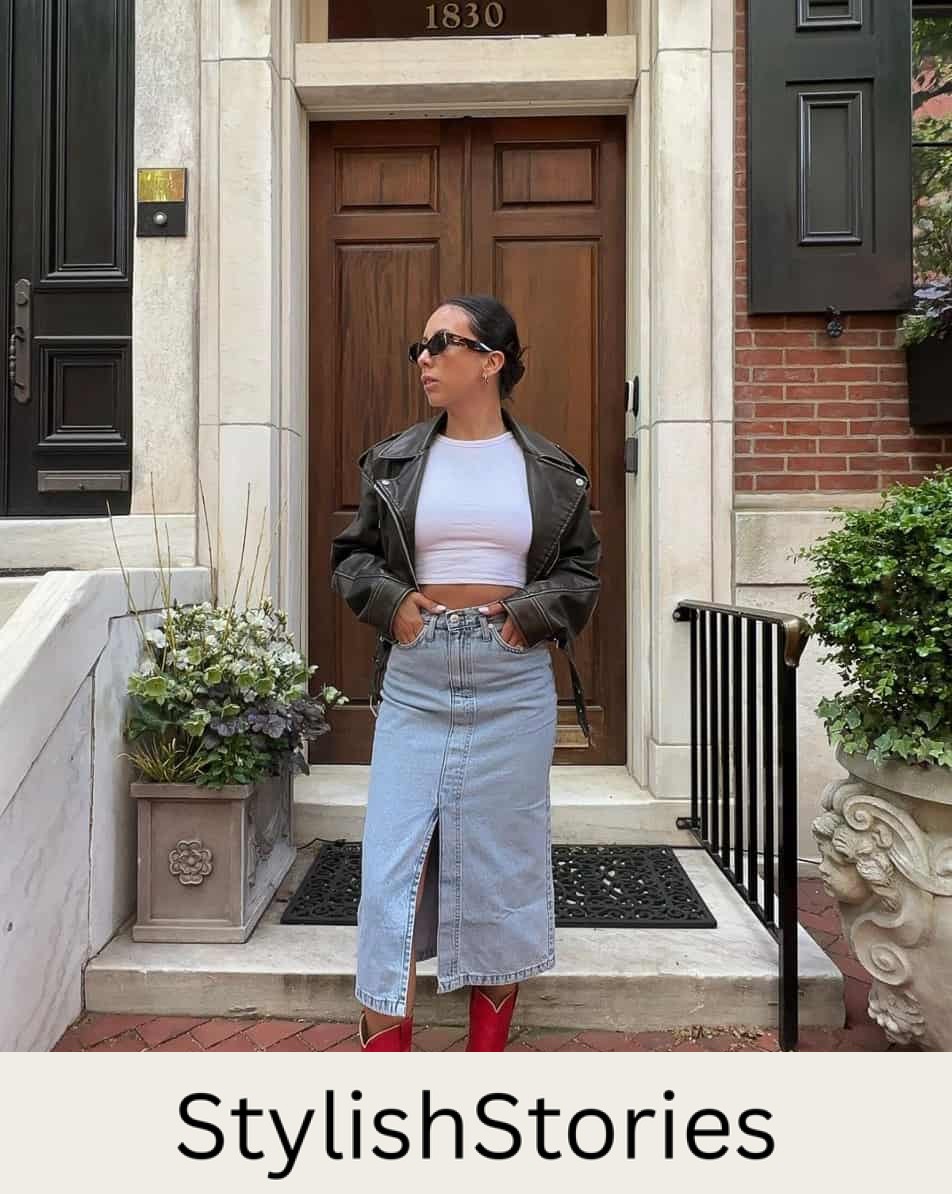 A woman wearing a denim midi skirt with a white crop top, a black leather jacket, and red cowboy boots