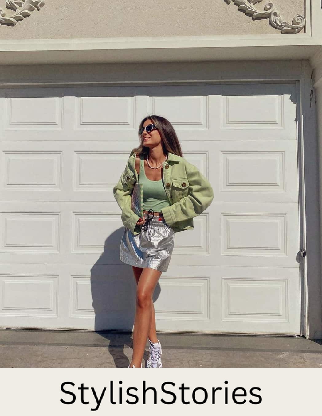 A woman wearing a silver mini skirt with a green tank top, a green jacket, and trainers