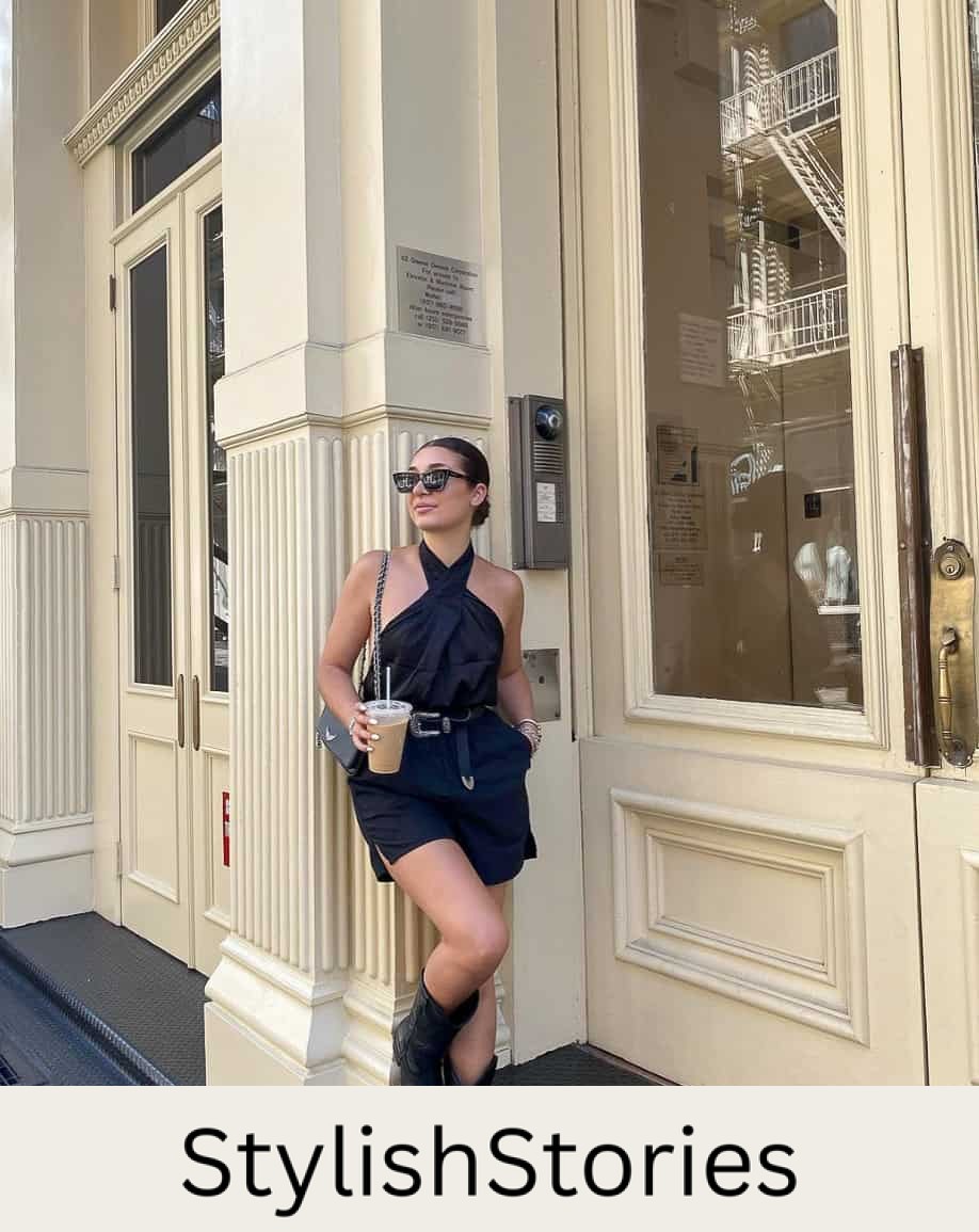 A woman wearing black shorts with a black halter top, black cowboy boots, black shoulder bags