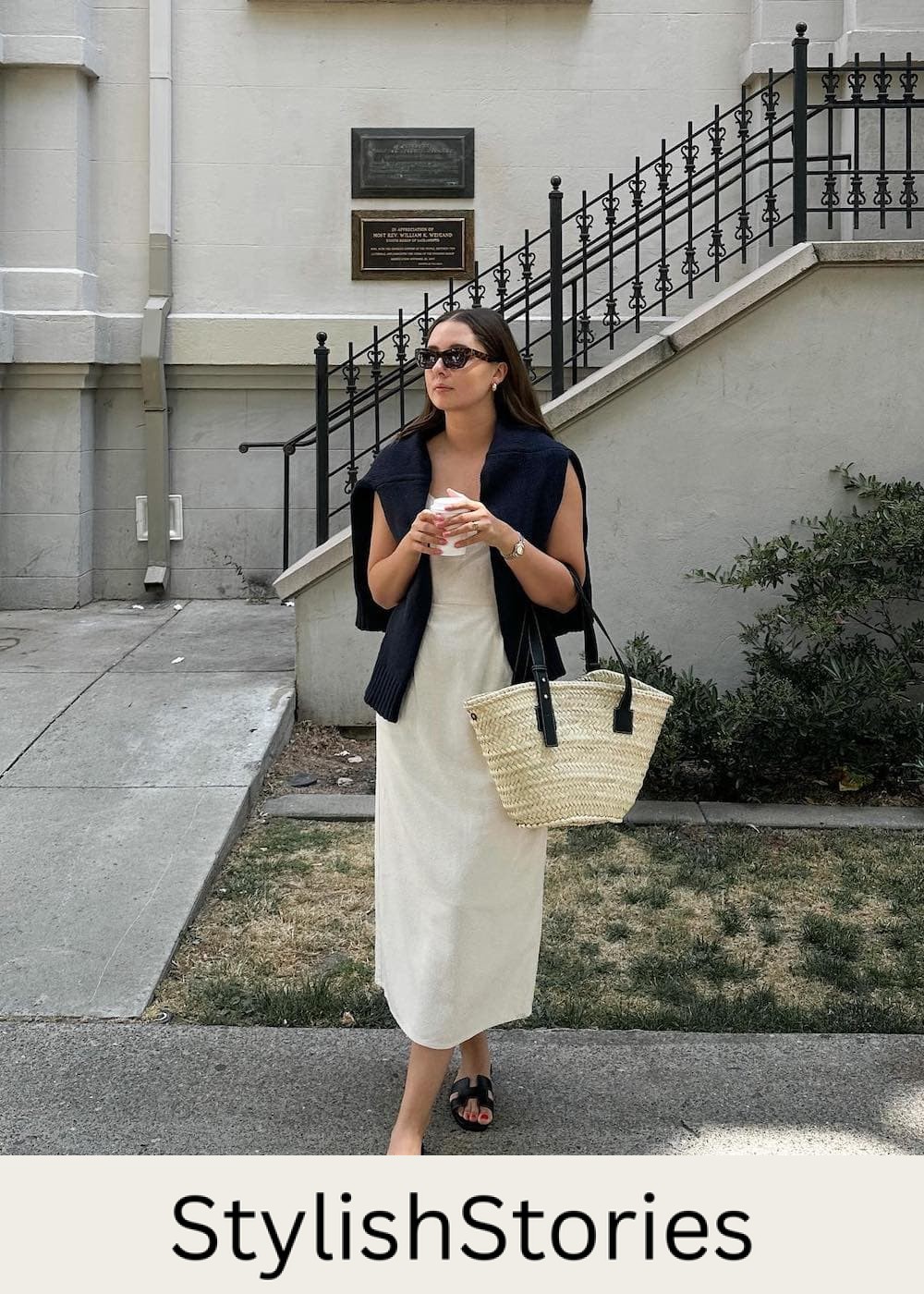 Woman wearing a cream midi dress with a black sweater over her shoulders and black sandals.