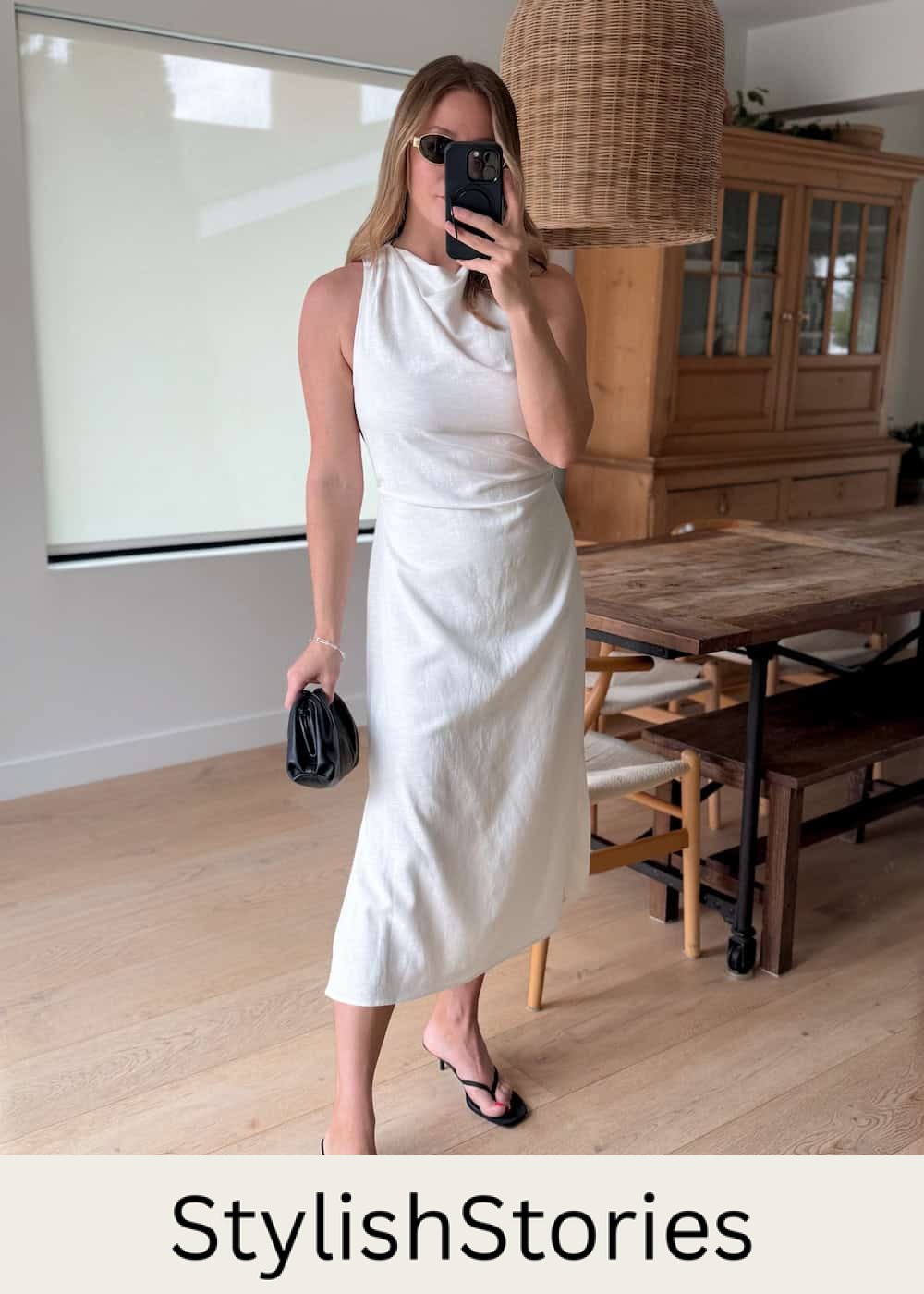 Christal wearing a white midi dress with black heeled sandals and black accessories.