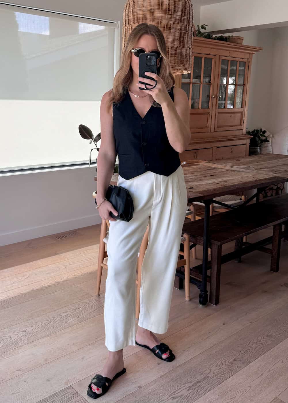 Christal wearing white, tailored pants with a black vest top and black sandals.
