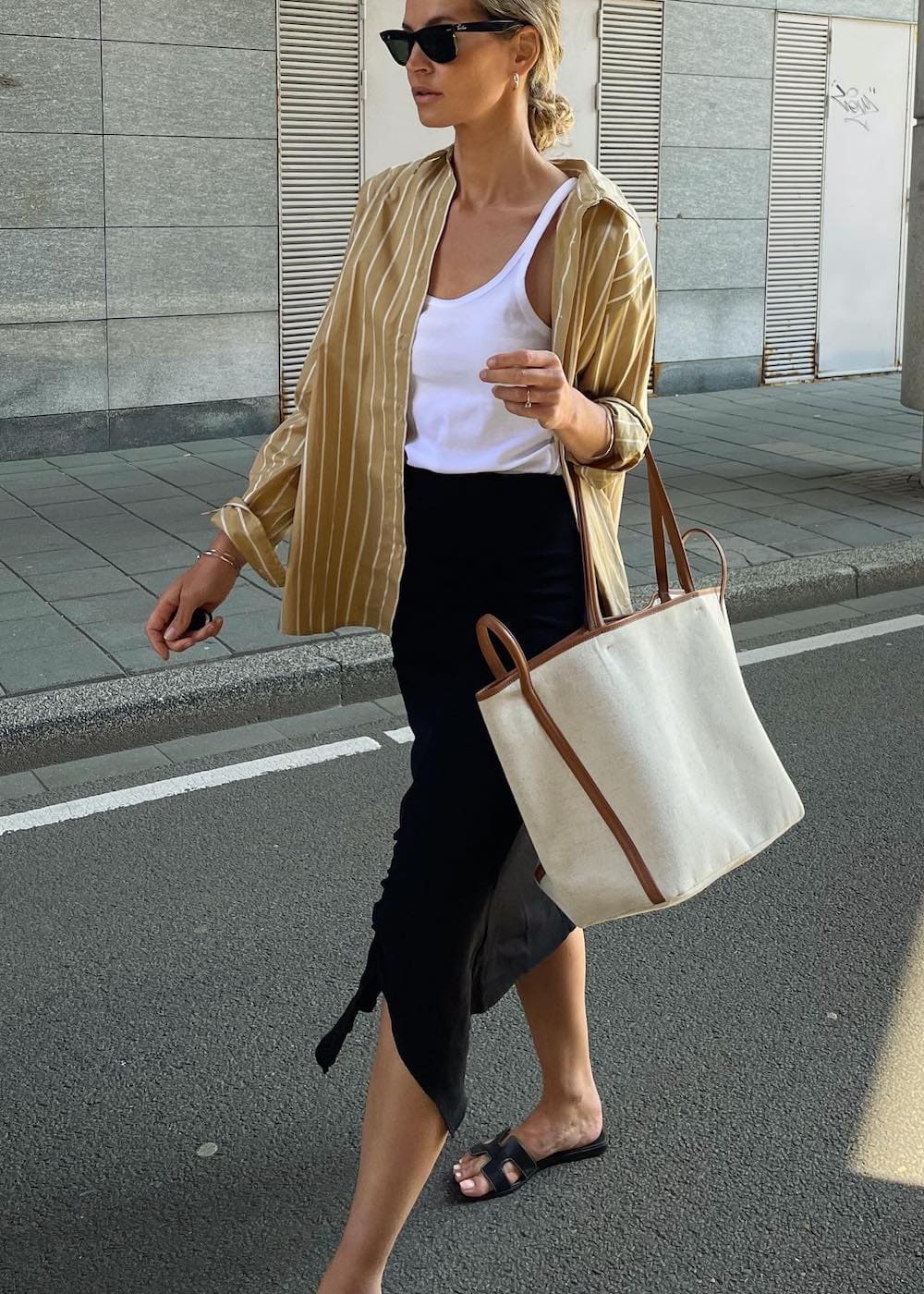 Woman wearing a black midi skirt with a white tank top and an oversized button down with sandals.