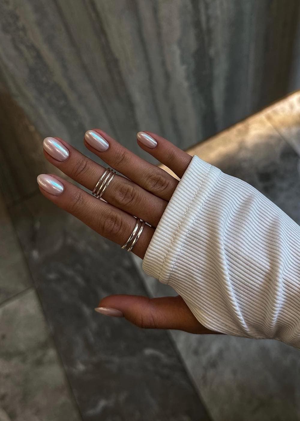 A closeup shot of a woman's hand with a fresh, chrome manicure and ring stacks.