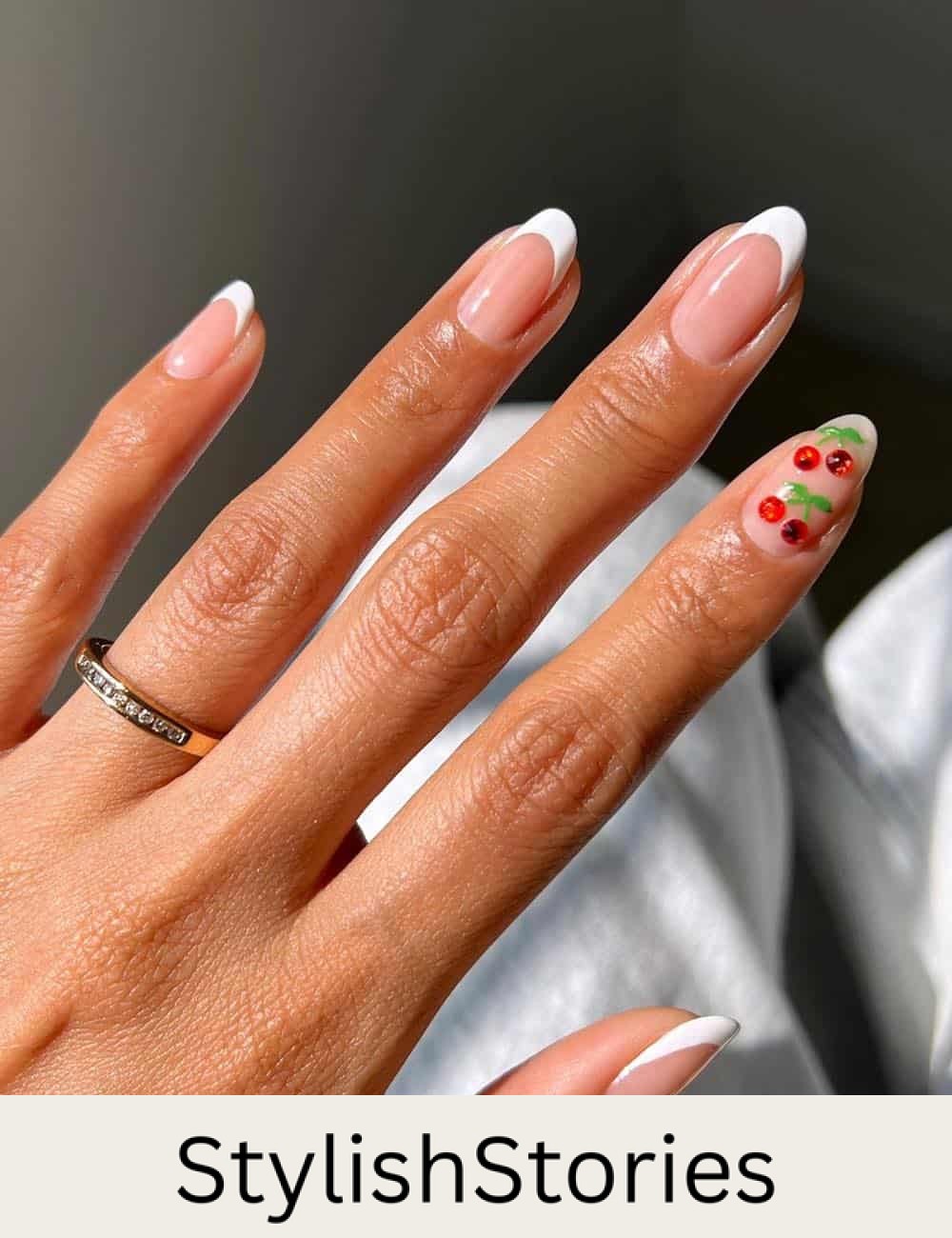 short round nude nails with white tips and an accent nail featuring cherry crystals