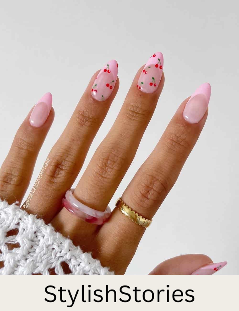short nude pink almond nails with pink tips and two accent nails with cherry patterns