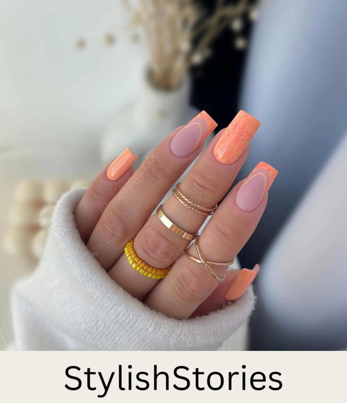 A hand with medium square nails featuring a mix of solid colored orange nails and matte nails with orange French tips