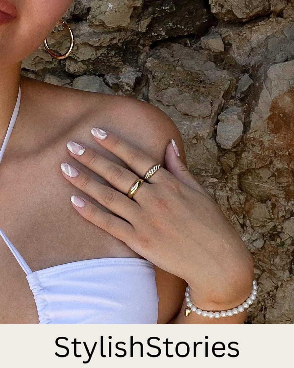 An up-close image of a woman's nails featuring nude pink polish and white wave accents