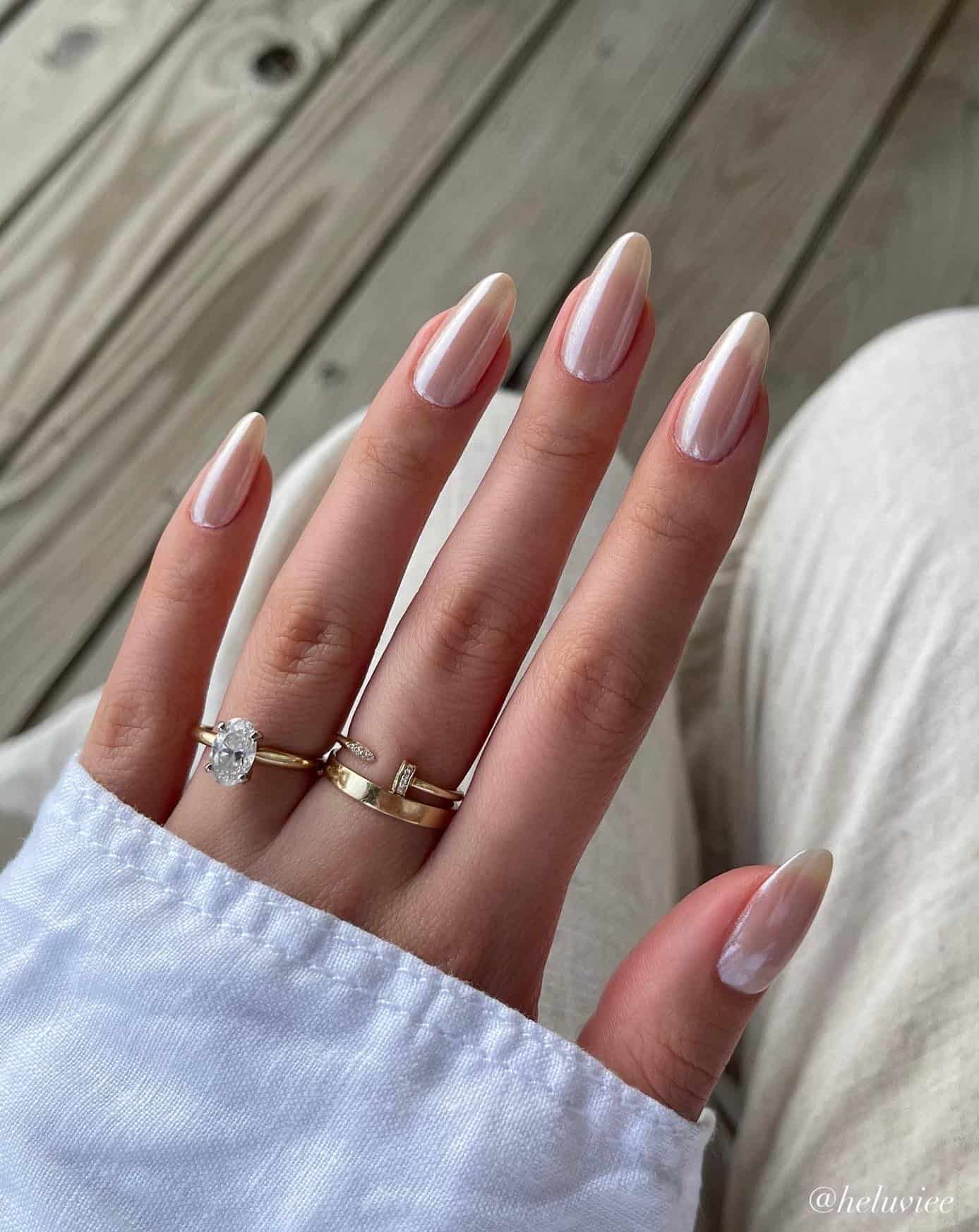 A hand with medium almond nails painted with a milky white polish and a chrome finish