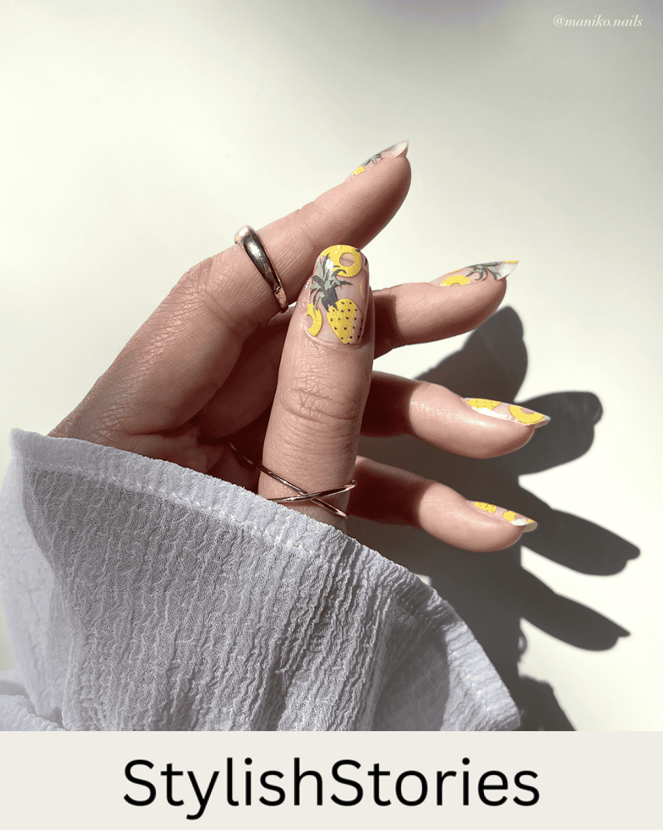 A hand with short squoval nails with a clear coat and painted with pineapple nail art