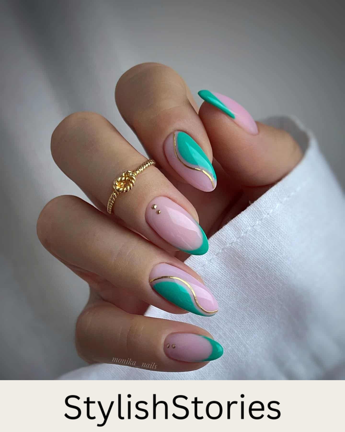 A hand with medium almond nails painted a light pink with green wave accents, green French tips, and gold line details