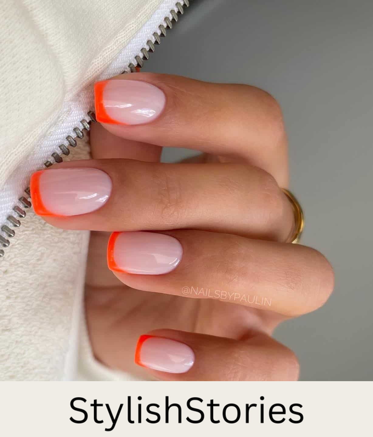 A hand with short square nails painted a pinkish nude tone with bright orange French tips