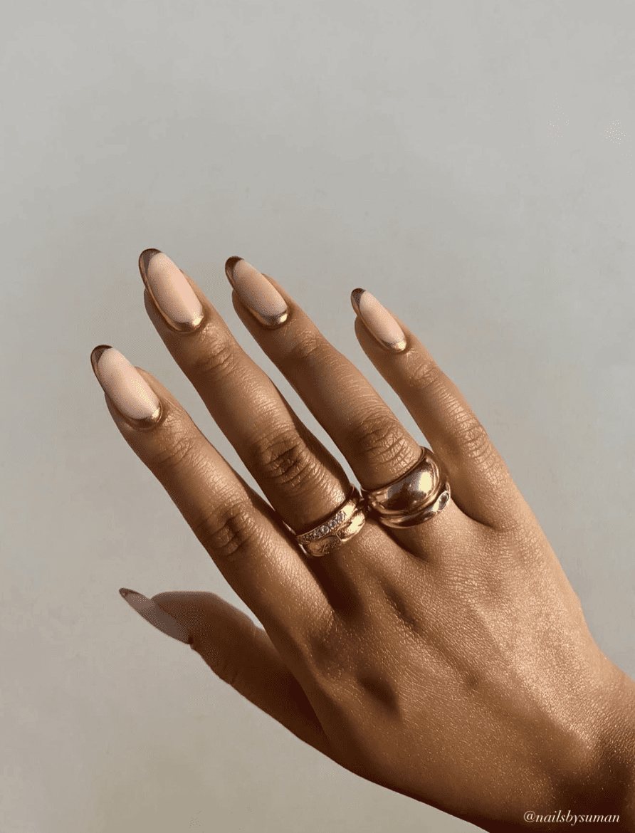 A hand with medium round nails painted a matte nude tone with gold polish outlining each nail