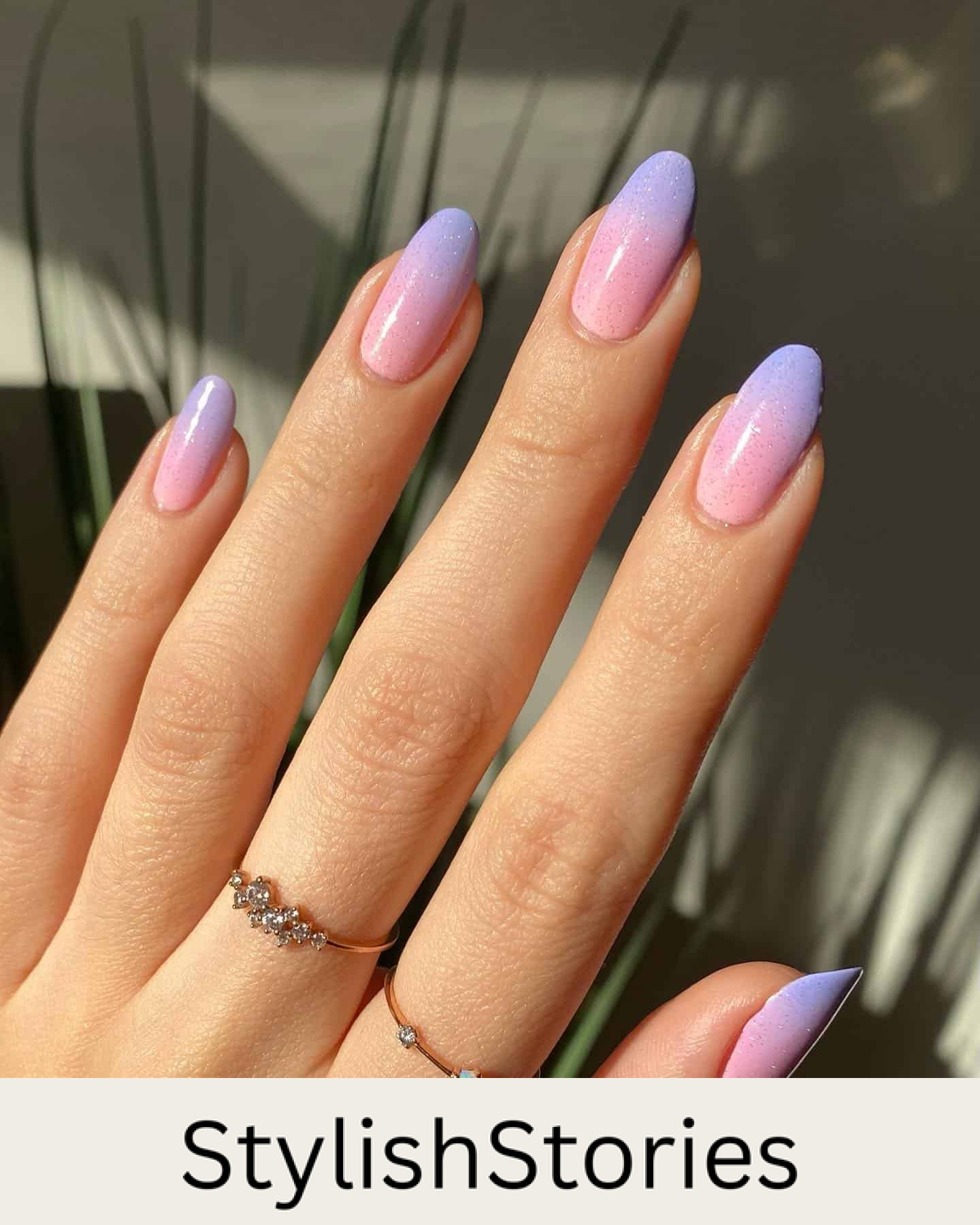 A hand with medium almond nails painted with a pink and purple ombre design and a glittering topcoat