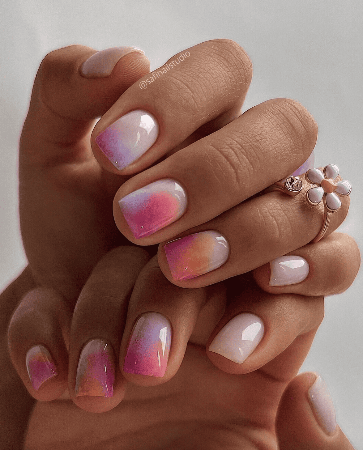 A hand with short square nails painted a milky white color with blue, purple, pink, and orange ombre nails
