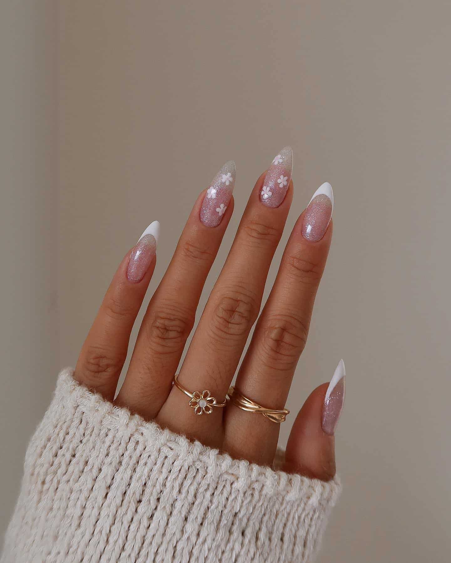 A hand with medium almond nails with a sparkly clear coat, white French tips, and two accent nails with white flowers