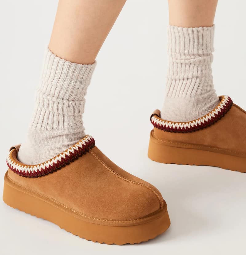 image of a woman's feet wearing brown suede slippers with red stitching and a faux shearling lining