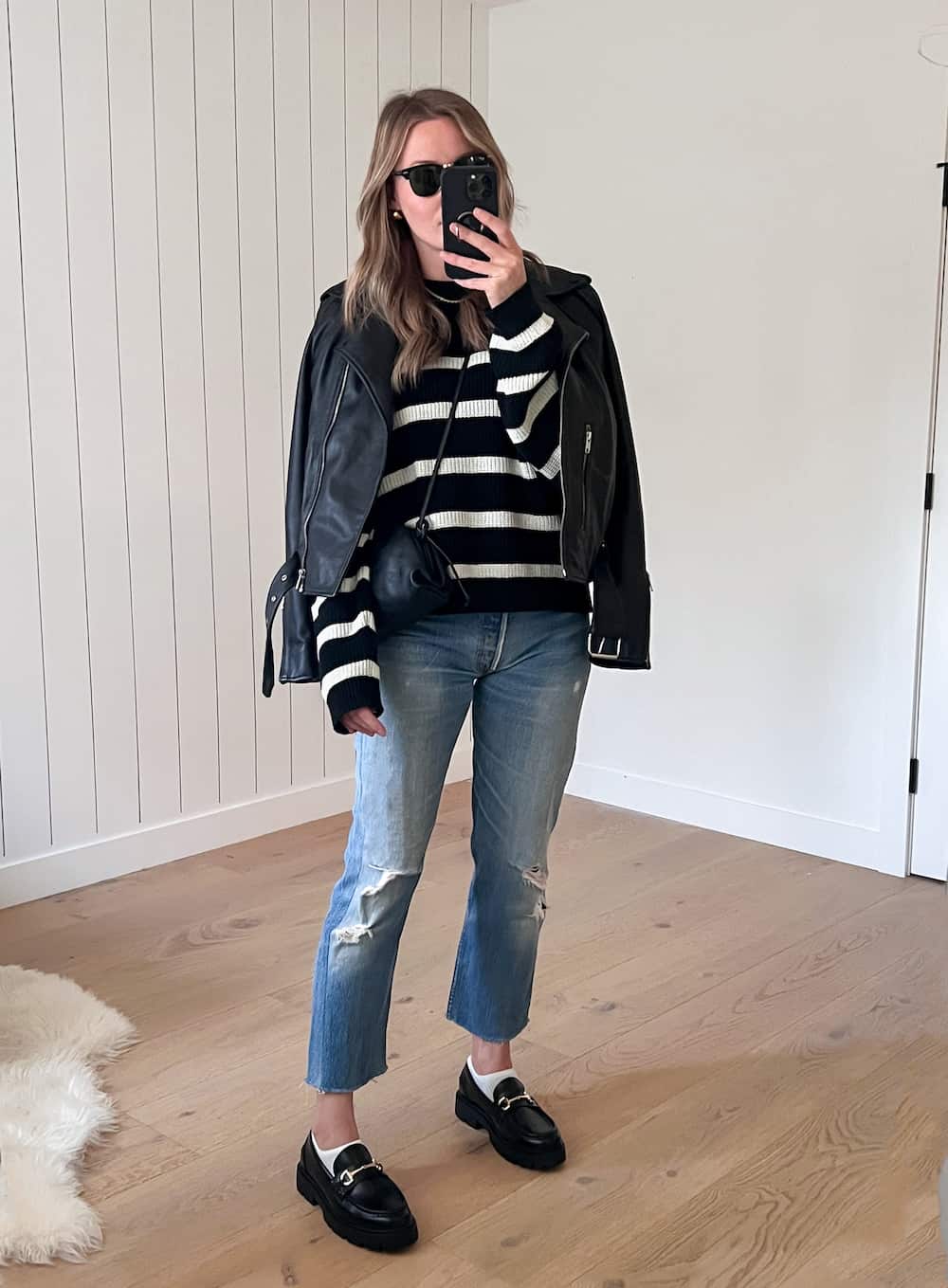 Christal wearing distressed jeans, black loafers and a black and white sweater under a leather jacket.