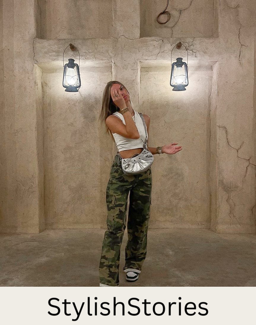 A woman wearing camo pants with a white cropped tank top, black and white sneakers, and a metallic silver purse
